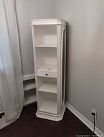 White rotating jewelry cabinet, corner wall placement, front view showing four shelf sections and one drawer.