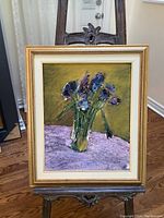 Full view of original signed floral painting in gilded frame on easel, showing the composition and colors.