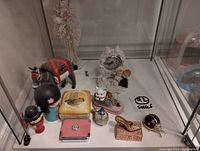 Photo showing various small collectible figurines including a clock figure, donkey, cat figurine, decorative boxes, and small dolls.