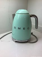 Front view of turquoise SMEG kettle showing logo and cord at base
