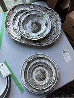 Nine antique porcelain pieces including platters, plates, and bowls arranged on a table; showing brown transferware floral and scenic decoration