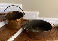 Photo showing both antique copper cauldron and washtub on wooden stairs, highlighting size and handle types.