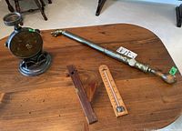 Antique metal sprayer with wood handle, family scale, wooden level, and thermometer displayed on wooden table.