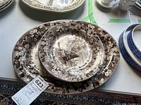 Three antique Wedgwood plates stacked with floral bordered brown transferware pattern depicting sailing ships and buildings.