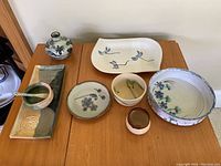 Overview of all eight pottery pieces laid out on a wooden table showing varied colors and shapes including plates, bowls, a vase, and a tray.