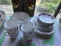 Photo showing stack of plates (side and dinner) and saucers with bowl and cups in front on white table near door.