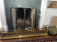 Full view of the brass fireplace screen with triple panels, the brass fireplace border in front and part of the tools set beside it.