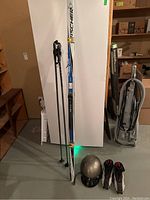 Full view of the cross country skis, poles, boots, and helmet arranged on a basement floor area with shelving and vacuum in background.