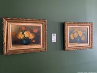 Photo of both framed oil paintings hanging on a green wall, showing overall appearance and matching ornate frames.