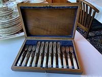 Wooden box open showing full set of six fish knives and six fish forks with mother-of-pearl handles inside blue velvet lining