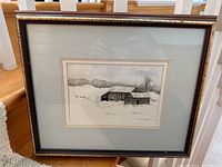 Full framed watercolour painting showing rustic barn in snowy field with light blue matting and dark frame.