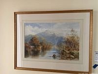 Full shot of the framed watercolor landscape painting showing river, trees, hills and mountains.