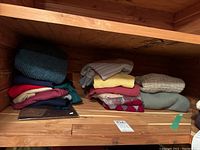 Photo of folded wool and cashmere sweaters stacked on wooden shelves showing variety of colors and materials.