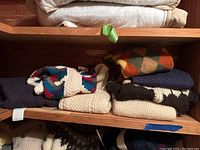 Five folded sweaters on wooden shelf, assorted patterns