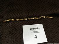 Full view of twisted rope style 10k gold chain necklace laid on dark textured fabric with MaxSold number card for scale.
