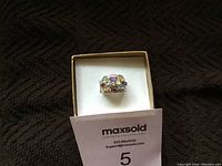 Front view of a sterling silver ring with multicolored precious stones displayed in a box with a MaxSold card.