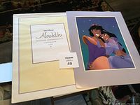 Walt Disney Aladdin exclusive commemorative lithograph with folder and certificate of authenticity seen on a dark patterned carpet.