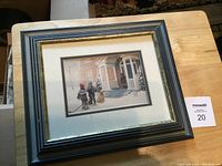 Photo of framed winter scene artwork showing children playing in front of a house on a snowy day.
