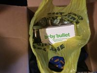 View down into yellow plastic bag containing Baby Bullet branded box and blending cups with lids inside a cardboard moving box.