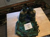 Front view of 10x50 camouflage binoculars resting on a wooden table with the camouflage carrying case beneath.