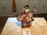 Front view of porcelain figurine of woman in flowing traditional dress holding a fan and trailing ribbon, on wooden table.