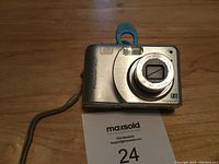 Front view of the silver HP Photosmart M627 digital camera showing the lens and some wear marks.