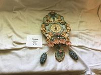 Full view of vintage cherub wall clock showing 3D cherub figures around central clock face with pine cone pendulums.