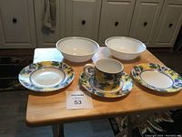 Photo of entire set showing two bowls, two plates, cup, and saucer with fruit pattern on wooden table, highlighting pattern and condition.