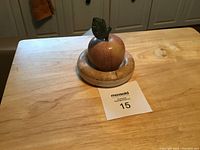 Photo showing a reddish-brown alabaster decorative apple with green leaf, seated on a beige alabaster circular base with natural patterns.