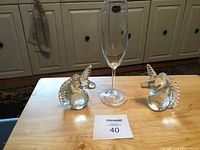 Two clear crystal unicorn head bookends and a clear crystal wine glass on a wood surface.