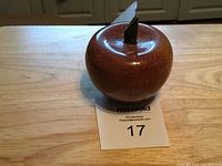 Red marble apple-shaped crystal paperweight on wooden table with maxsold lot card number 17.