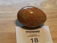 Top view of polished peach moonstone crystal egg resting on wooden surface with MaxSold lot card.