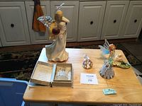 Full view of five fairy-themed statues and figurines on a wooden surface against white cabinetry backdrop