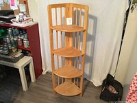 Front view of the four-tier pine folding plant stand positioned in a corner against a white backdrop, showing the overall structure and shelves.