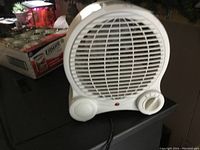Front view of small white portable fan heater with circular grill and control dials.