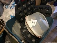 Overview of muffin tins, overlays of baking molds, and plastic cake carrier arranged in storage bin.