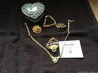 Photo of entire set on black fabric showing silver-tone heart jewelry box and five pieces of gold-tone jewelry including necklace, brooches, and pendants.