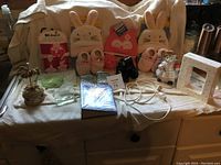 Wide view of kids' hats and booties, decorative doll, lamp frame, shoes, music box, key holders, and cloths on display surface