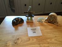Four decorative items on a wooden table: black sleeping cat, stacking stones sculpture, jade elephant figurine, and ornate mini mantle clock; all in used condition.