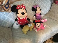 Three Minnie Mouse plush dolls of varying sizes and outfits on a couch.