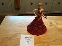 Porcelain Royal Doulton Pretty Ladies Special Celebration figurine in red dress with gold sash, standing on a wooden table.