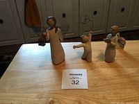 Three Willow Tree figurines displayed on a wooden surface with an auction lot number card, including an adult angel, child with balloon, and child angel with bird.