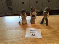 Three Willow Tree figurines arranged on a wooden table, with catalog number in frame for auction.