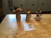 Three Willow Tree angel figurines on wooden surface with auction lot number 34 card.