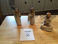 Three Willow Tree angel statues on wooden surface, viewed from front showing poses and materials.
