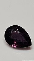 Close-up image of the single pear-shaped deep pinkish purple sapphire showing facet reflections and color under direct light.
