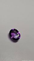Photo of an oval cabochon cut amethyst gemstone showing deep purple color and polished smooth surface.
