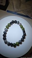 Top view of the gemstone bracelet showing chunky black, green, and patterned beads on a white surface.