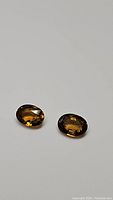 Photo showing two oval cut golden tourmaline gemstones on a white background, highlighting their color and faceted cuts.