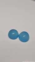 Pair of round cabochon natural chalcedony stones with icey blue color on white background.